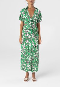 Groene bloemenjurk met korte mouwen, strik aan de voorkant, met witte en lichtgroene bloempatronen op een donkergroene achtergrond.