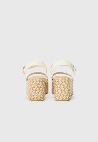 Sandales compensées blanches à lanières avec talons en jute tressé. L'arrière présente un design texturé et tressé avec des brides de cheville ajustables.
