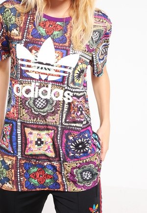 Kolorowa, wzorzysta koszulka z wielobarwnymi kwadratami i kwiatowymi wzorami. Białe logo Adidas na klatce piersiowej. Krótki rękaw.