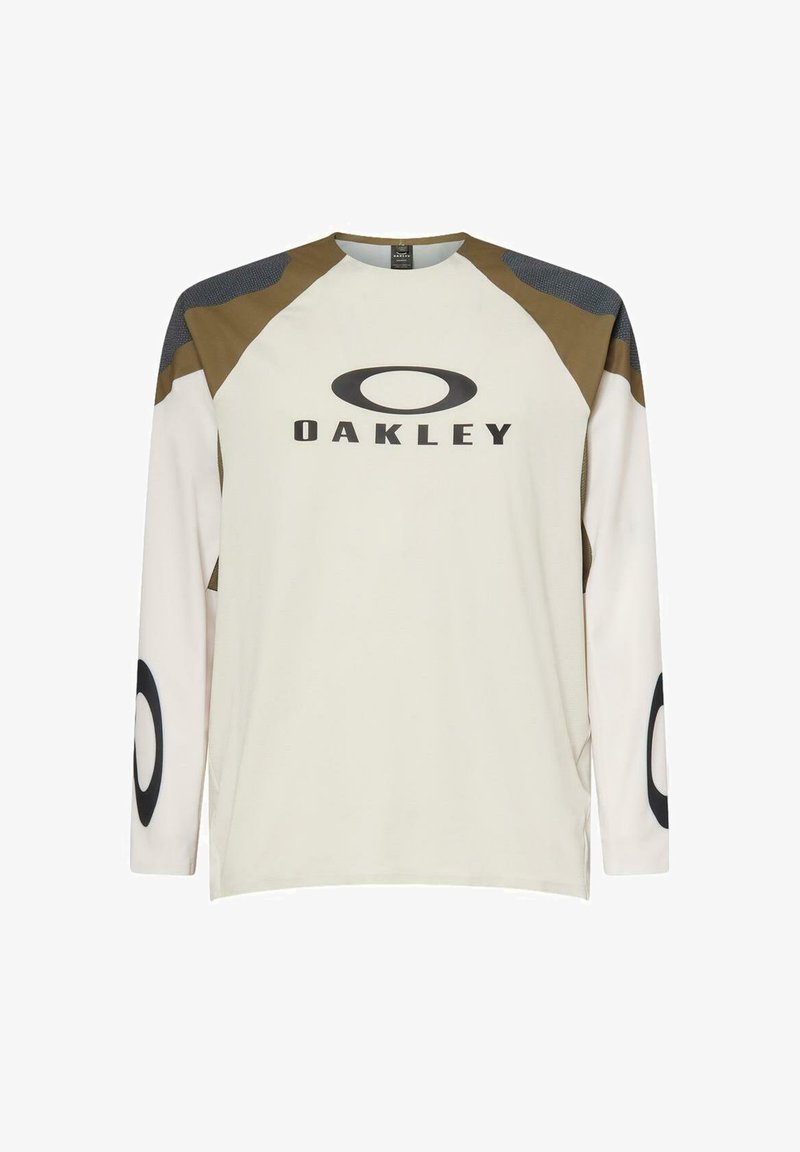 Camiseta beige de manga larga de Oakley con paneles en los hombros marrón y gris oscuro, logo en el pecho y logos circulares en las mangas.