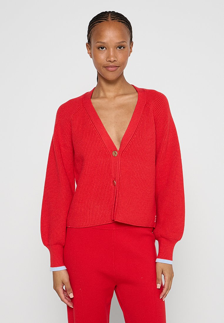 Roter gerippter Cardigan mit tiefem V-Ausschnitt, langen gepufften Ärmeln und einem einzigen goldenen Knopfverschluss, kombiniert mit passenden roten Hosen.