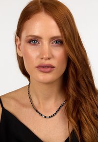 Collana nera e argento con maglie quadrate e rettangolari, caratterizzata da una texture liscia e una finitura lucida, indossata su clavicole scoperte.