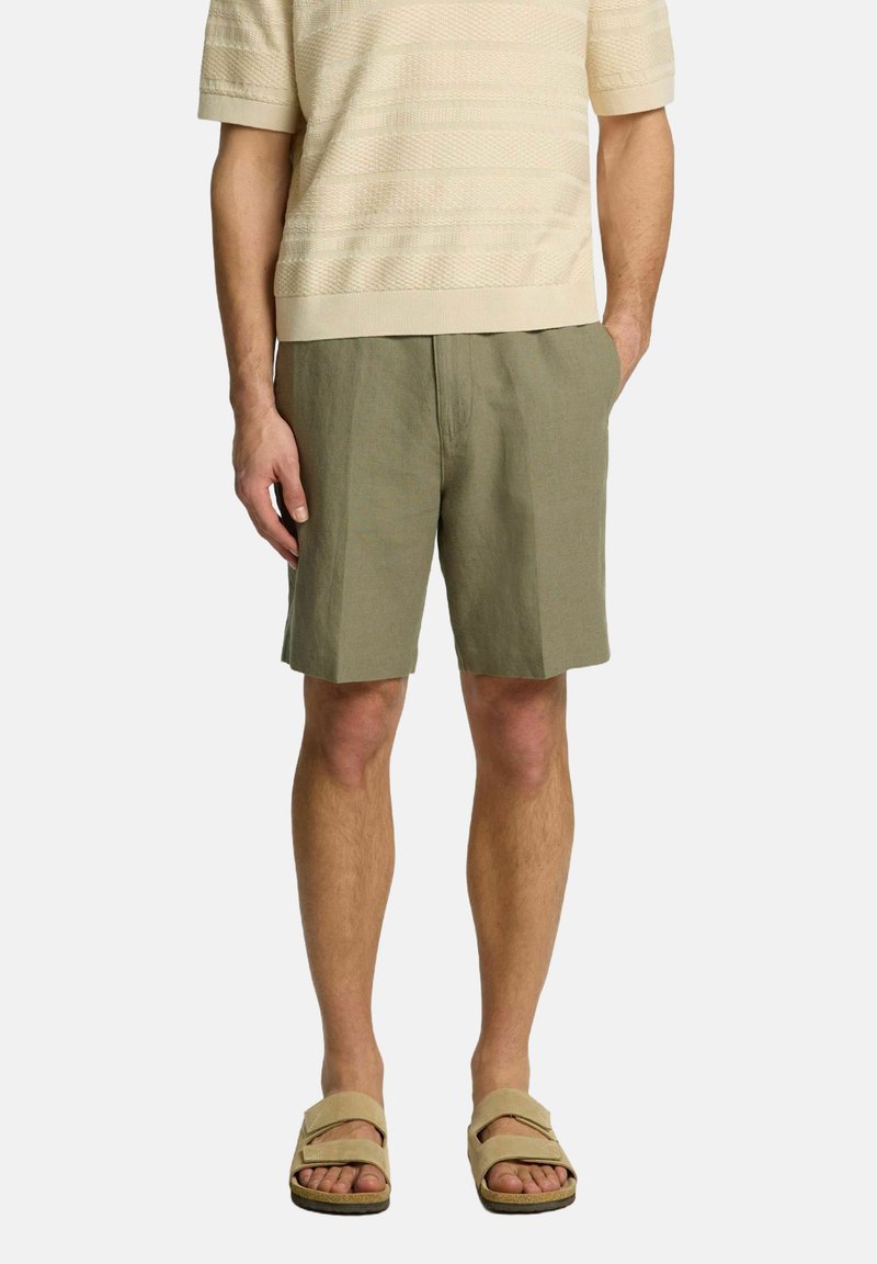 Oluļu zaļi lina šorti ar brīvu piegriezumu, kas aprīkoti ar priekšējām kabatām un gludu, teksturētu virsmu. Apvienoti ar vieglu, teksturētu krējuma krāsas krekla.