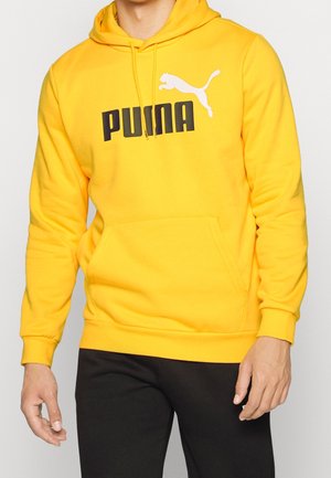 Mand iført en skarp gul Puma-hoodie med frontlomme og sort Puma-logo, kombineret med sorte bukser.