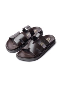 Braune Rutschsandalen mit zwei breiten Riemen, aus glattem synthetischem Material, mit einer schwarzen Sohle und goldfarbenen Logodetails auf der Innensohle.