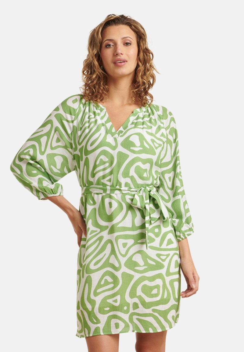 Groene jurk met een V-hals, lange mouwen en een strikceintuur, versierd met abstracte vormen in verschillende tinten groen en wit.