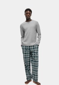Gray long-sleeve shirt paired with green and white plaid pajama pants. Pants feature an elastic waistband with drawstring. Model is barefoot.