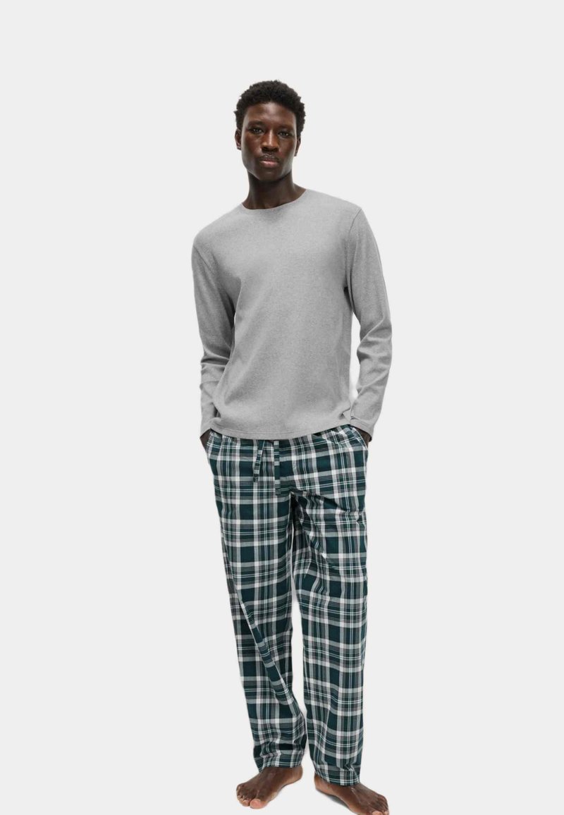 Gray long-sleeve shirt paired with green and white plaid pajama pants. Pants feature an elastic waistband with drawstring. Model is barefoot.