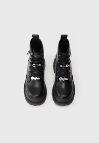 Μαύρες δερμάτινες μποτες με κορδόνια και χοντρές σόλες, διακοσμημένες με ασημένιες ασφάλειες και κρεμαστά κωδικών της μάρκας στα κορδόνια.