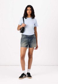 Lichtblauw geribd gebreid t-shirt, versleten korte denim shorts, zwarte sneakers met witte accenten, met een kleine zwarte handtas.