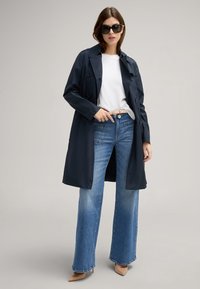 Granatowy trench coat z podwójnym zapięciem noszony na białej bluzce, zestawiony z jasnoniebieskimi spodniami typu wide-leg i cielistymi szpilkami z ostrym noskiem.