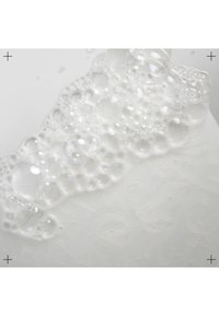 Heldere vloeistof met schuimige witte bellen op een gestructureerd oppervlak, dat een ingewikkeld patroon onder de bellen toont.