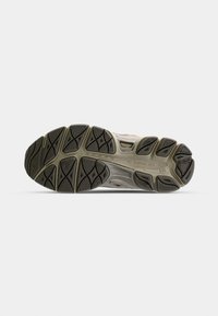 Semelle d'une chaussure de course grise et noire usée montrant les motifs de la semelle et les textures sur un fond plat gris clair.