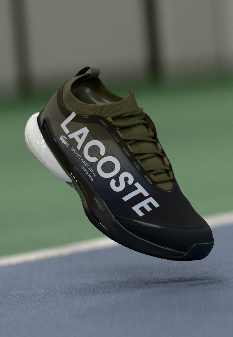 Crne i maslinaste atletske tenisice s mrežastim gornjim dijelom, istaknutim bijelim logotipom "LACOSTE" i elegantnom, fleksibilnom potplatom za bolje performanse.