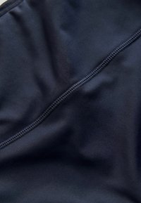 Prim-plan cu o țesătură închisă la culoare, cu cusături strânse și uniforme de-a lungul unei cusături, evidențiind textura și detaliile materialului.