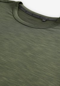 T-shirt verde con texture, scollo tondo e tessuto morbido e leggero. Presenta un motivo sottile e dettagli neri lungo il scollo.