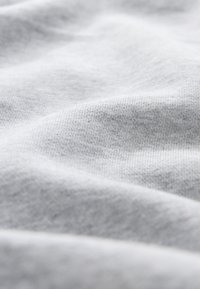 Tessuto grigio chiaro con una trama liscia e morbida, caratterizzato da sottili motivi di intreccio e pieghe che creano profondità e dimensione.