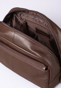 Brown leather bag with a smooth texture, featuring a zippered main compartment and an additional front pocket. Lined interior, no patterns.