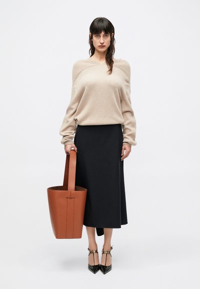Béžový sveter s rebrovanými ramenami, čierna midi sukňa, hnedá kožená taška tote a čierne špicaté topánky s členkovými remienkami.