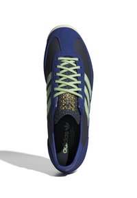 Adidas sneaker cu un exterior din suede albastru și sintetic, șireturi verzi și trei dungi verzi. Detaliu auriu accentuat pe limba încălțămintei.