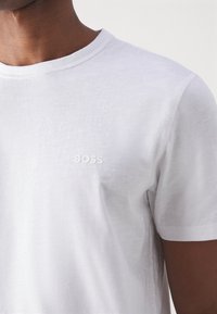 Weißes T-Shirt mit kurzen Ärmeln aus weichem Stoff, mit einem dezenten geprägten Logo "BOSS" auf der Vorderseite, Rundhalsausschnitt und glatter Textur.