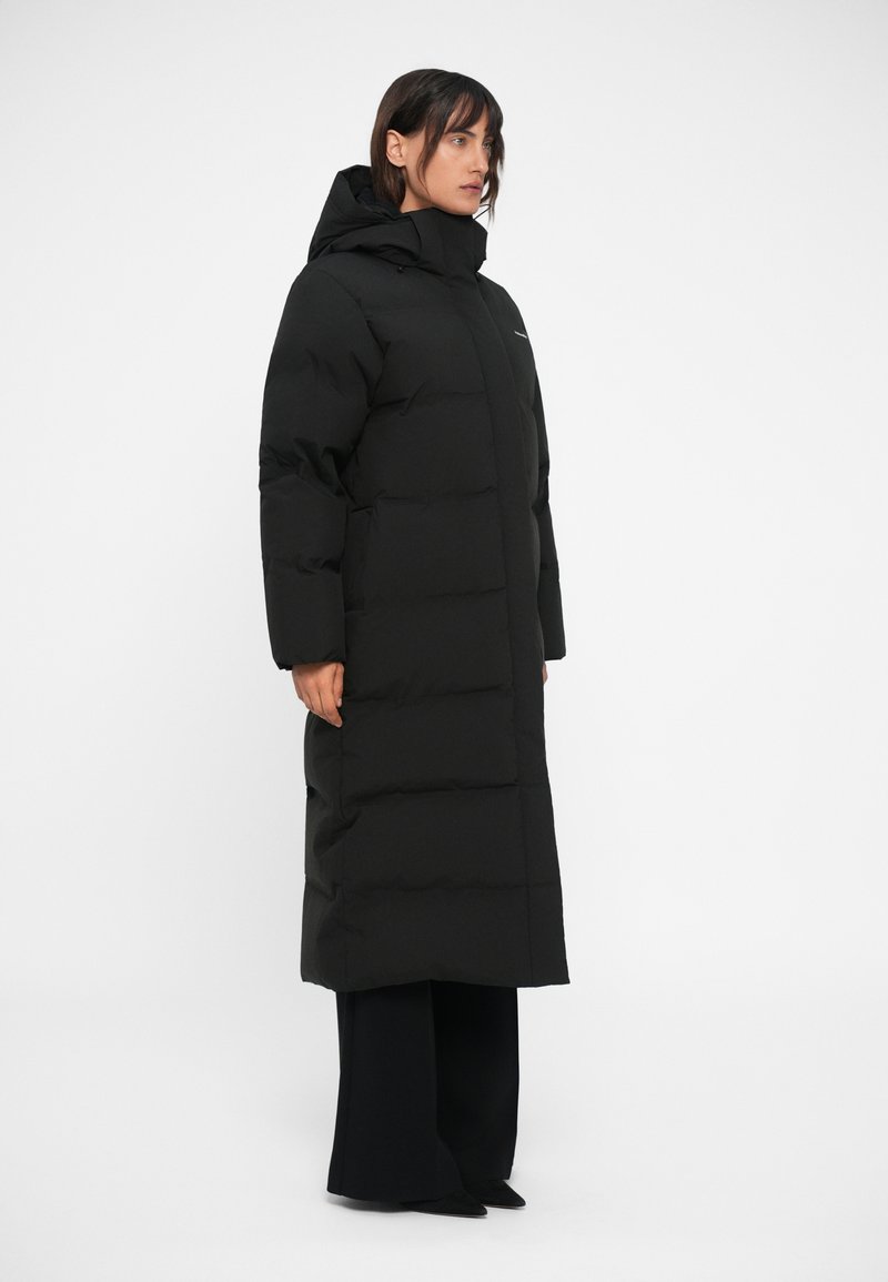 Long black puffer coat with a hood, featuring a quilted pattern, a high collar, and long sleeves. Material appears smooth and insulated.