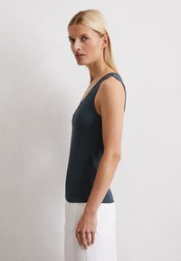 Donkerblauw aansluitend mouwloos shirt met een diepe V-hals en brede banden, van gestructureerde ribstof, gecombineerd met witte high-waisted broeken.