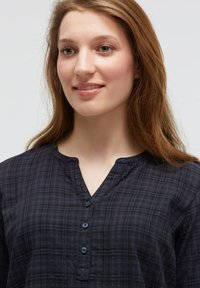 Dunkelkarierte Hemd mit Knopfleiste und V-Ausschnitt, das eine subtile Textur und weichen Stoff aufweist. Beinhaltet vier Knöpfe entlang der Frontleiste.