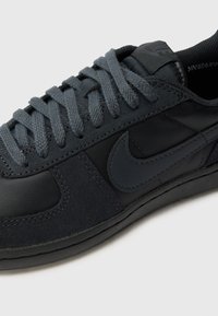 Basket Nike noire avec des lacets gris foncé, des détails en cuir et en daim, et le logo Nike swoosh sur le côté.
