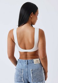 Top corto bianco a coste con spalline larghe e schiena bassa. Indossato con pantaloni shorts in denim azzurro chiaro con tasche in pizzo e una fascia con marchio.
