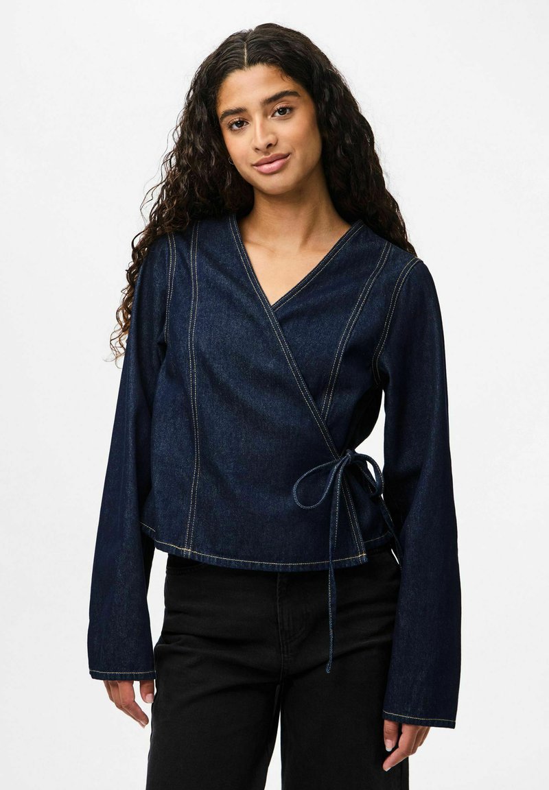 Top avvolgente in denim blu scuro con maniche lunghe, scollatura a V e dettaglio di legatura in vita. Presenta cuciture a contrasto e un design corto.