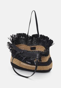 Woven torba tote w czarno-beżowe paski z frędzlami, czarnymi skórzanymi uchwytami i białym nadrukiem z przodu.