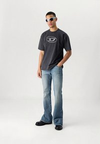 Γκρι γραφικό t-shirt, ανοιχτό μπλε παντελόνι καμπάνα, μαύρα παπούτσια και γυαλιά ηλίου. Βαμβακερό υλικό με άνετη εφαρμογή και στρογγυλή λεπτομέρεια λογότυπου στο πουκάμισο.