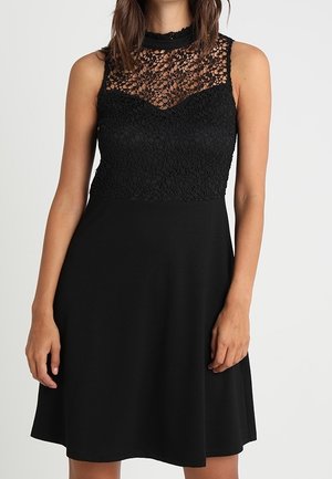 Robe noire avec un bodice en dentelle et une jupe unie. Conception sans manches avec un col haut. Texture lisse sur la section jupe.