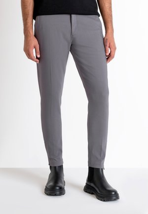 Pantalones grises ajustados de corte entallado, confeccionados en una tela suave. Incluyen bolsillos frontales y una línea de planchado en cada pierna. Se llevan con botas negras de tobillo.