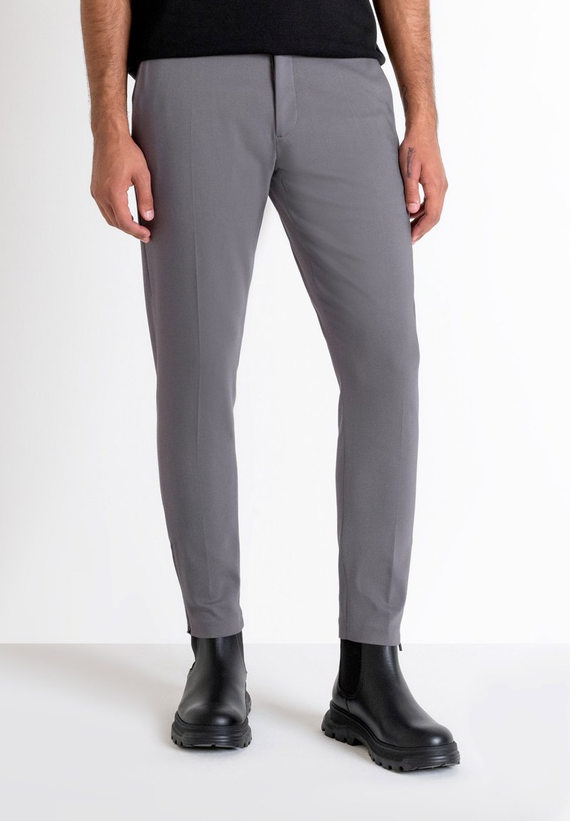 Pantalones grises ajustados de corte entallado, confeccionados en una tela suave. Incluyen bolsillos frontales y una línea de planchado en cada pierna. Se llevan con botas negras de tobillo.