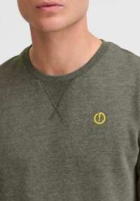 Dark green sweatshirt with a crew neckline, featuring a small yellow embroidered logo on the chest and ribbed cuffs and hem.