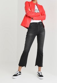 Veste en cuir rouge, t-shirt graphique blanc, jean noir taille haute avec ourlet brut, et baskets noir et blanc.