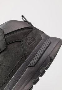 Bottes noires jusqu'à la cheville alliant cuir lisse et daim, dotées de semelles en caoutchouc robustes et d'un logo bien en vue.