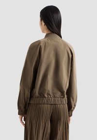 Giacca bomber in tessuto marrone con orlo e polsini arricciati, presenta un colletto semplice e una finitura liscia, vista da dietro.