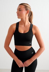 Svart atletisk crop top med ribbet tekstur, firkantet utringning og brede stropper, kombinert med høytaljede ribbede leggings. Ingen synlige logoer.