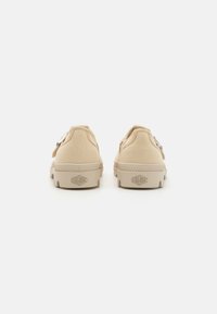 Zapatillas de lona beige con un acabado texturizado, puntera redonda y suela de goma. Cuenta con una pestaña trasera y el logo "Palladium" en el talón.