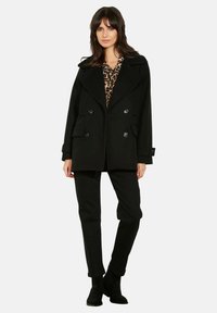 Schwarzer Peacoat mit doppelreihigen Knöpfen, weitem Kragen und zwei Fronttaschen, kombiniert mit schwarzen Hosen und einem Leopardenmuster-Oberteil.