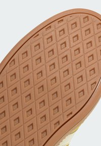 Sko sula med ett texturerat brunt gummimaterial med ett rutmönster som ger grepp och flexibilitet. Kurvad kant för ergonomisk design.