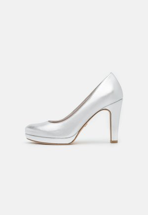 Sølv højhælet pumpe med en slank, blank overflade, rund tå og en platform-bund. Hælen er tykkere med et let guld-accent.