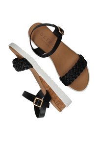 Sandales noires tressées avec semelle intermédiaire en liège et semelle blanche. Bandes avec boucles dorées. Semelle intérieure texturée et branding subtil sur la semelle.
