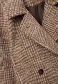 Brauner karierter Wollmantel mit Reverskragen, doppelter Knopfleiste und strukturiertem Finish mit sichtbaren Nähten und einem schwarzen Knopf.