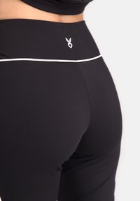 Mustad kõrge vöökohtaga mustad legginsid, millel on valge aktsentjoon ja väike logodetail seljal. Siledast ja elastset materjalist.