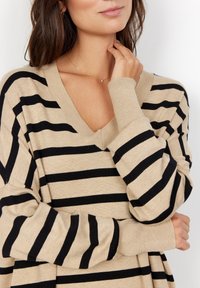 Beige en zwarte gestreepte oversized sweater met een V-hals, lange mouwen en geribde boorden. Zachte breisel stof met een ontspannen pasvorm.
