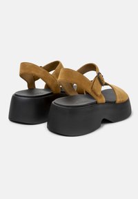 Hnědé semišové platformové sandály s kulatou špičkou, které mají design s křížovými popruhy a detail s přezkou, posazené na silné černé podrážce.